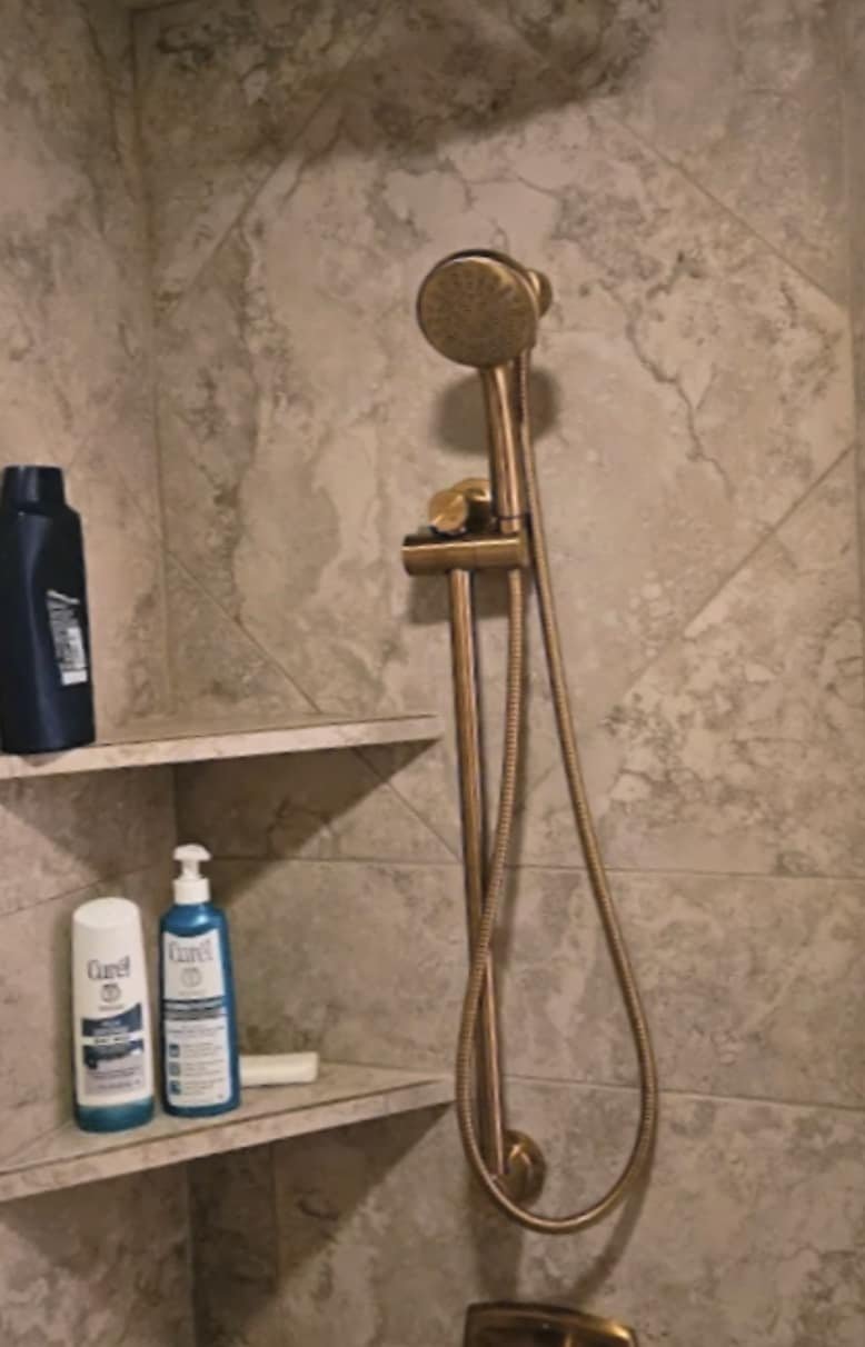 Brass handheld shower fixture on a tiled shower wall