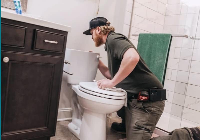 Plumber repairing a toilet in a home bathroom